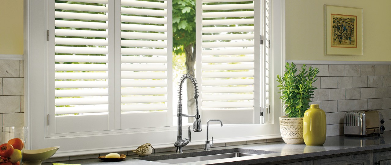 Kitchen sink in front of Hunter Douglas Palm Beach Shutters in white.